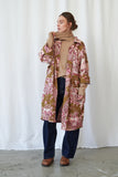 Woman wearing a patterned coat over a beige sweater with a white background