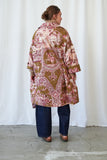 Person wearing a patterned coat standing against a white curtain