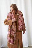 Woman wearing a patterned scarf and brown coat against a white curtain background