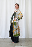 Woman wearing a long, patterned coat against a white curtain background