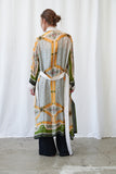 Person wearing a long, patterned coat with a white curtain background