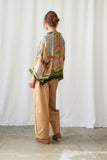 Person wearing a patterned top and beige pants against a white curtain background