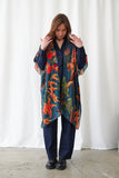 Woman wearing a colorful floral scarf over a dark outfit against a white curtain background