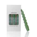 Green spiral candle in front of a Máegen packaging on a white background