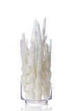 White twisted taper candles arranged inside a clear cylindrical glass container, photographed on a clean white background with a soft reflection below.