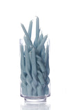 A clear cylindrical glass container filled with twisted, spiral-shaped candles in a pale dusty blue color, set against a seamless white background.